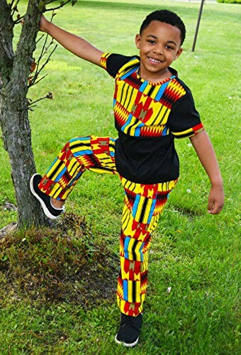 Child in a colorful traditional outfit standing by a tree on grass.