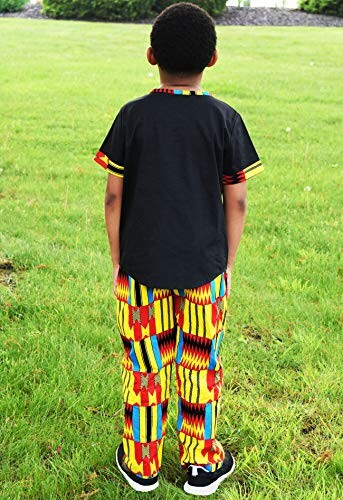 Child wearing colorful kente outfit standing on grass.